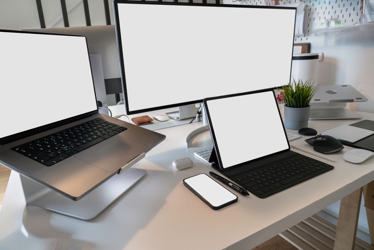 Un espace de travail propre et moderne avec un ordinateur portable, une tablette, un smartphone et un écran. Idéal pour le télétravail et les configurations technologiques.